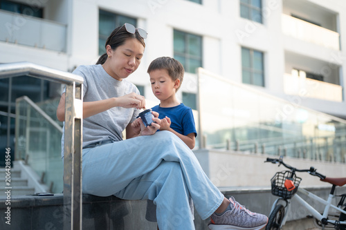Asian woman in her 30s enjoying ice cream with her 4-year-old son outdoors