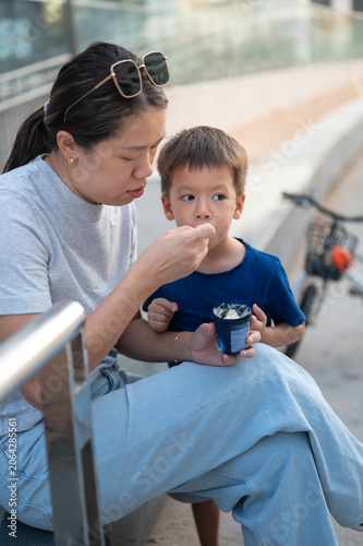 Asian woman in her 30s enjoying ice cream with her 4-year-old son outdoors