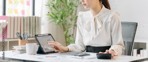 Bild auf Leinwand Financial Focus: A diligent businesswoman meticulously analyzes data on her tablet, surrounded by office supplies and a calculator, embodying concentration and professional dedication