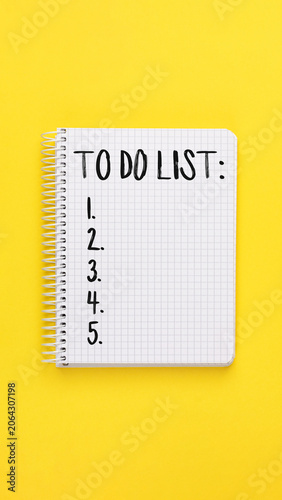 To Do List in white spiral notebook on bright yellow background. Blank lines for task entry with numbers one through five. Overhead view, planning concept