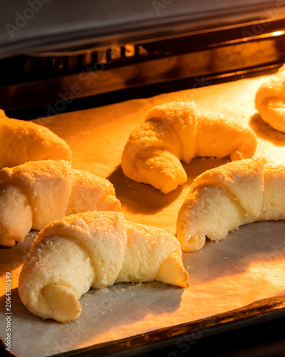 Fresh crescent rolls baking on parchment paper inside oven. Homemade pastry breakfast preparation