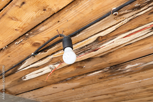 Bare old light bulb hanging from a rustic unfinished wooden ceiling. Industrial rustic style lighting in an old abandoned wooden building renovation. copy space.