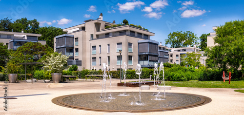 Immeuble résidentiel moderne haut de gamme bordant la fontaine du Pregny Parc sous un ciel d'été