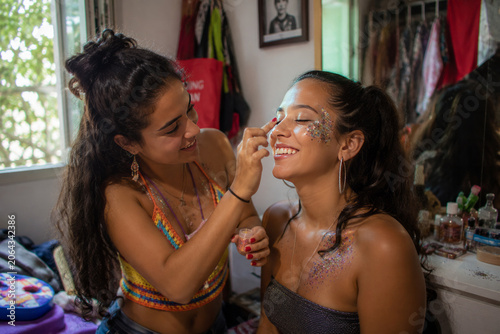 Young woman applying glitter makeup on friend's face