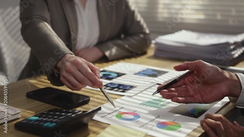 Close up of business people hands pointing at financial documents with charts and graphs during a meeting, analyzing company performance and discussing strategy in the office boardroom