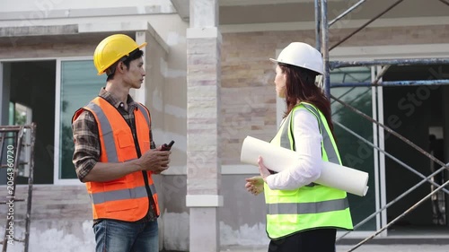 Professional female architect holding a blueprint and a male foreman discussing the project while standing at a residential building construction site