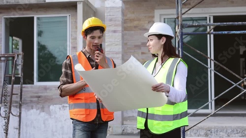 Professional female architect and male construction worker wearing safety gear, discussing project plans on a blueprint and shaking hands in agreement at a residential building site