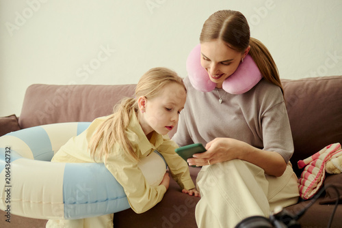 Caucasian mother and child checking smartphone while resting in hotel room during family trip, showing travel planning and vacation stay. Useful for tourism, hospitality, family travel ads