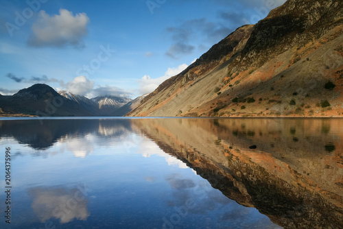 Calm mountain reflection on the mirror surface of Wastwater under a blue sky with soft white clouds