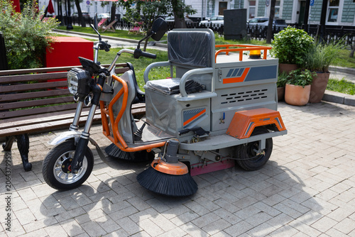 Compact electric street sweeper machine parked on city pavement, urban maintenance and public utility service