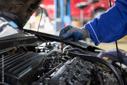 Worker checks oil level in car engine during maintenance session in garage