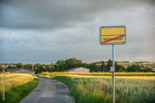 Hinweisschild Ortsende Mittelstadt vor Felderlandschaft mit Holzscheunen. Feldweg und Wolkenhimmel in Reutlingen-Mittelstadt