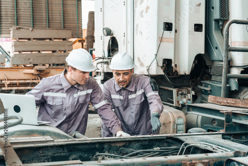 Two Caucasian Mechanics Checking Truck Engine Mechanical Parts with Laptop in Industrial Workshop Warehouse Facility