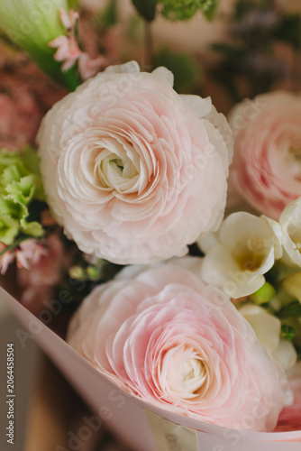 Close-up of a delicate wedding bouquet featuring pale pink ranunculus flowers and white freesia. Soft focus, pastel floral background.