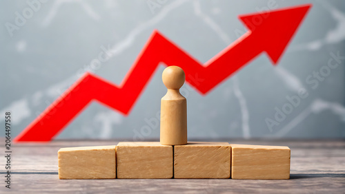A wooden peg doll standing on a stack of wooden blocks with a large red arrow pointing upwards in the background, representing business growth