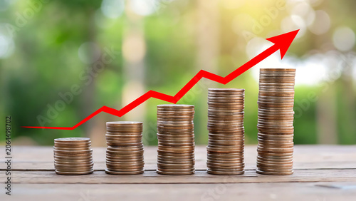Five stacks of gold coins of increasing height on a wooden table with a red arrow pointing upwards to symbolize financial growth and profit