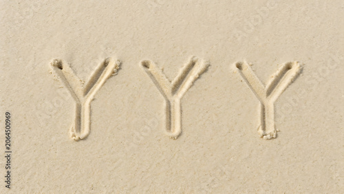 Three uppercase letter y characters written in the fine beige sand of a beach, view of handwritten alphabet letters on a sandy surface