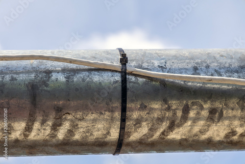 Industrial metallic pipe surface with cable secured using plastic zip tie