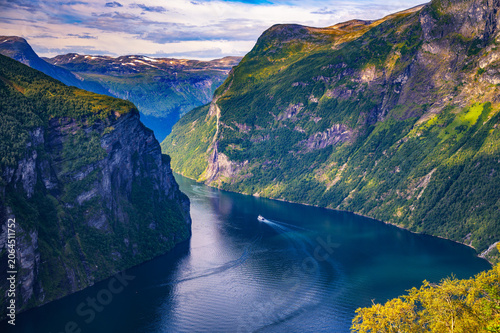 Photos Panoramic view of Geirangerfjord with the Seven Sisters waterfall, steep green cliffs and a small boat on calm blue water in western Norway