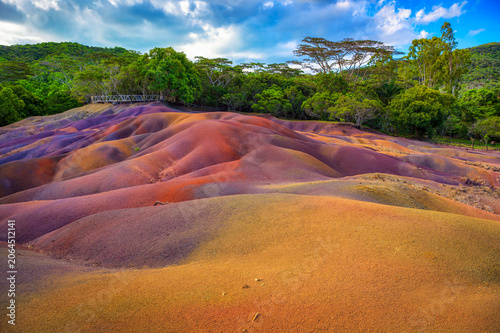 Chamarel, Riviere Noire, Mauritius - February 20, 2025 : Rippled, multicolored dunes of the Seven Colored Earth Geopark with lush rainforest backdrop under dramatic clouds.