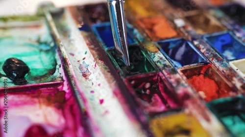 Paintbrush dipping into a green watercolor paint cuvette.