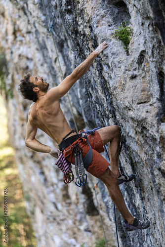 Billede på lærred Shirtless climber reaches for a handhold on a rugged rock face