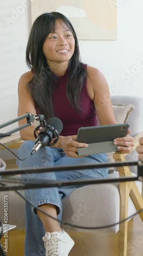 Vertical video: Replying to cue host in maroon top holding tablet speaking into mic in home studio
