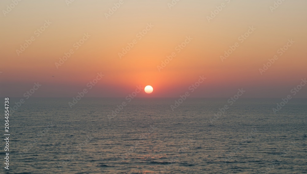 Obraz premium Sunset over calm ocean waters with orange sky
