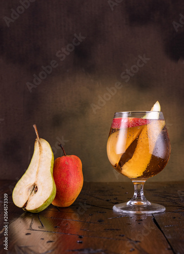 Wine glass with drink, apple and pear slices, fresh cut fruit nearby, pear cut lengthwise on vintage brown background, rustic concept.