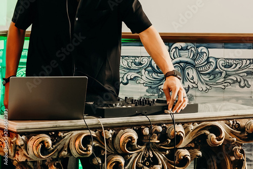 DJ mixing music in a lively setting while using turntables for  crowd at  local event in evening.  His hands are actively adjusting equipment. venue has  vibrant atmosphere,  is enjoying performance