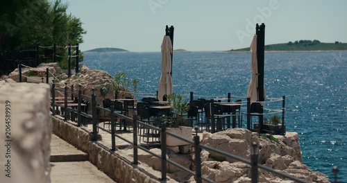 An outdoor terrace with tables and umbrellas overlooks the Adriatic Sea and distant islands near Primosten, Croatia.