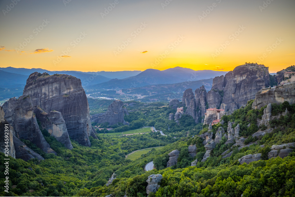 Obraz premium Spectacular sunset view from a viewpoint overlooking Meteora in Greece. Warm golden and orange light bathes the towering sandstone rock formations and historic Orthodox monasteries