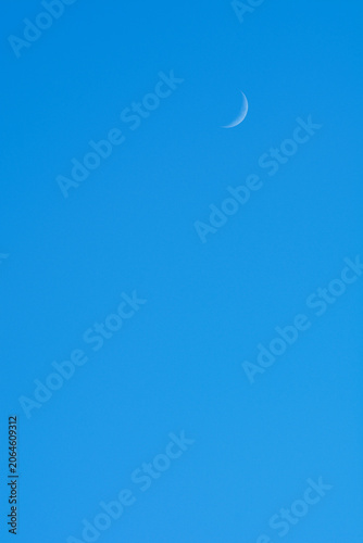 Minimalist view of a slender young moon during daytime