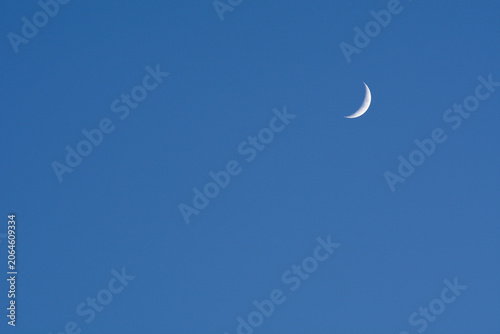 Waxing crescent moon shining against a bright blue daylight sky