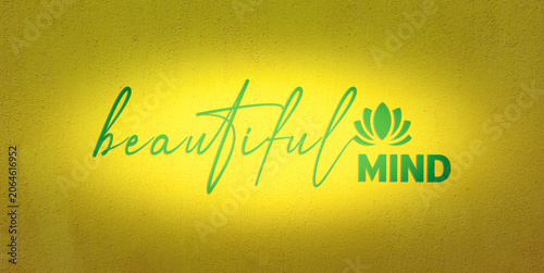 Inspirational green Beautiful Mind text with a lotus flower icon on a textured yellow concrete wall background with central light spot suitable for mental health banner or yoga design.