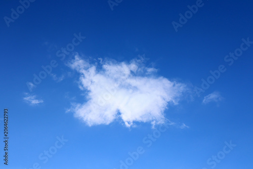 A lone cloud in the blue sky. A clear blue sky with one white fluffy cloud. A fair-weather cumulus cloud.