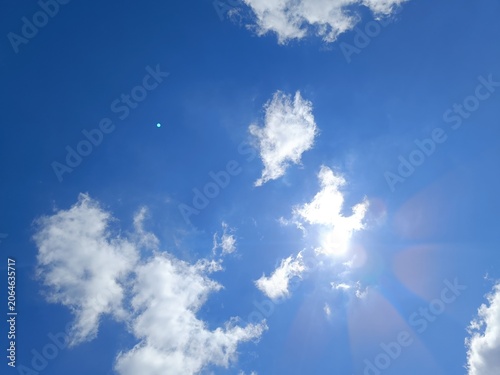 Bright blue sky with fluffy white cumulus clouds. Sun shining brightly creating a sunburst and lens flare effect. Copy space for text