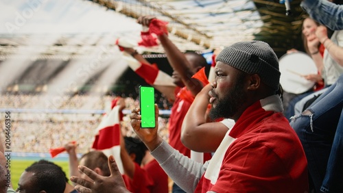 Obraz na płótnie Vertical mockup screen on phone held by soccer fan in the stadium stands during world championship football match, Energetic cheering crowd at authentic sports event full of pride with isolated