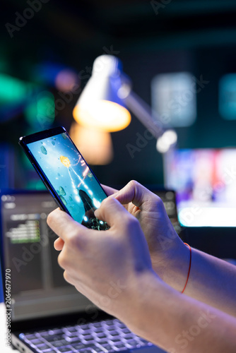 Selective focus of a person holding a cell phone and playing video games. Closeup of an individual entertaining oneself with a space shooter game on a mobile device.