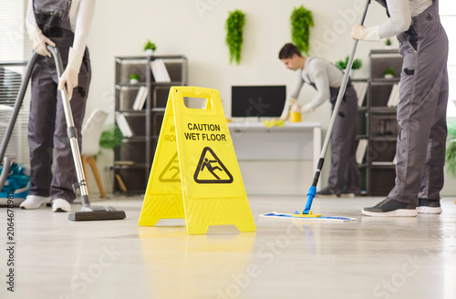 Cuadro en lienzo Cleaners janitors team mopping office with caution cleaning