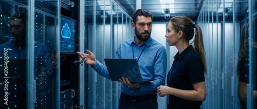 Male it specialist and female technician discussing work in a data center with cloud visualization.