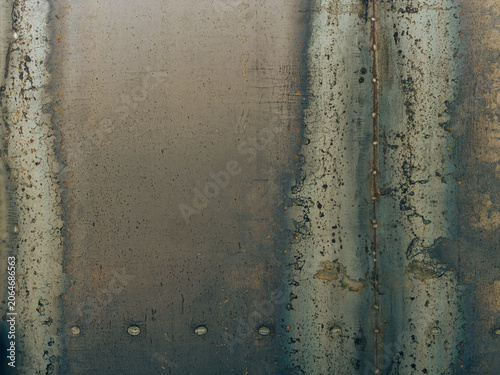 Weathered industrial metal sheet with rustic patches, oxidation, and visible welding seams, creating a dark, textured, and raw metallic background surface