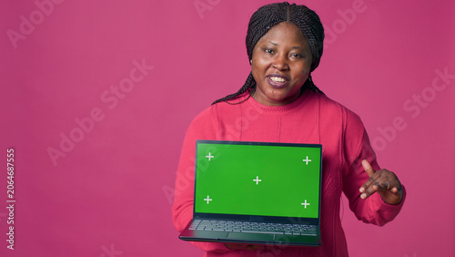 Young lady with African American ethnicity grasping laptop showcasing isolated chromakey template, with minicomputer with mockup green screen display held by beautiful Black woman.