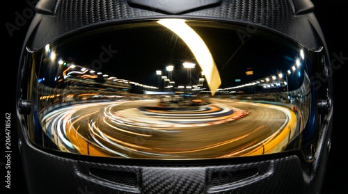 Close-up of a professional helmet with night racing reflection. Speed ​​movement of a racing circuit in the visor of a carbon fiber helmet.