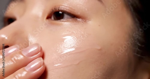 Young Asian woman applying moisturizing face serum to her cheek skin