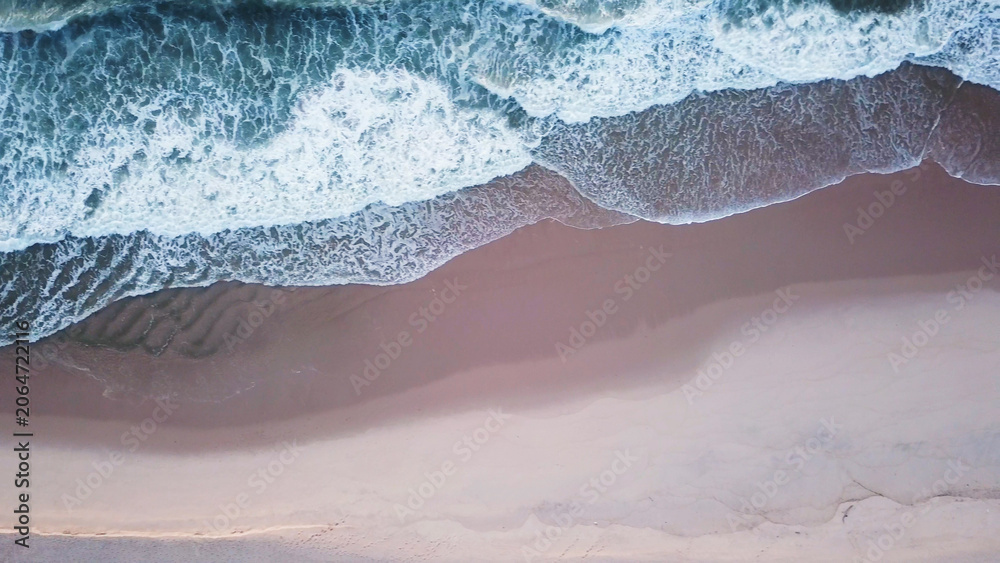 Obraz premium Aerial view of ocean waves hitting a sandy beach