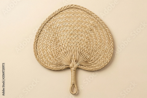 Woven natural palm leaf hand fan on a beige background