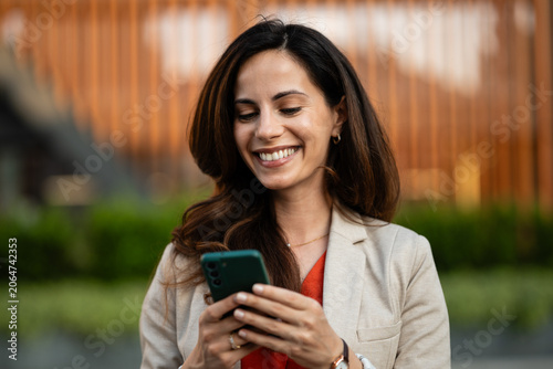 Cuadro en lienzo Woman smiling using smartphone, communicating outdoor in city