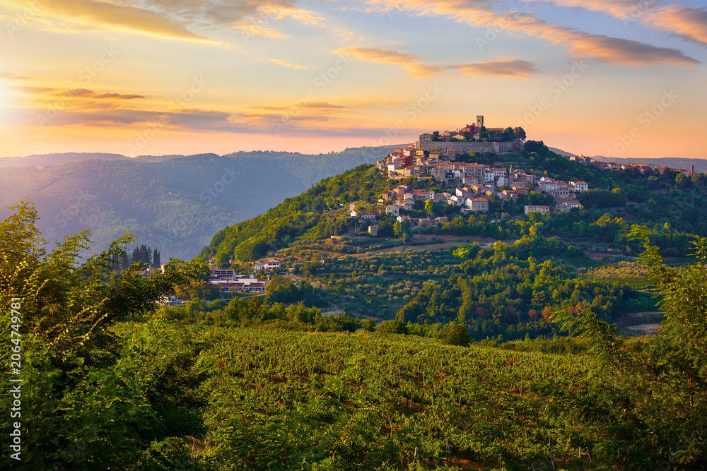 Obraz premium Antique city Motovun Croatia Istria. Picturesque panorama age-old village at hill with pink cloud and sunny light and authentic home with red tegular roof and green vineyard garden.