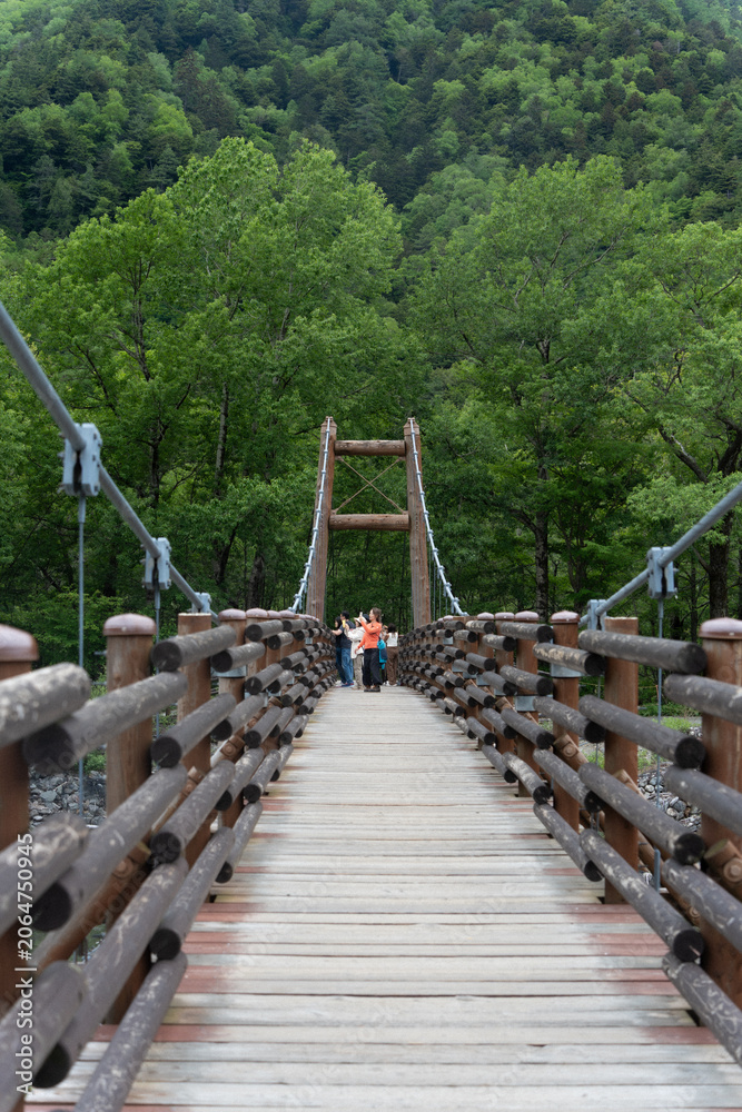 Obraz premium Suspension bridge over river surrounded by mountains, Kamikochi, Japan